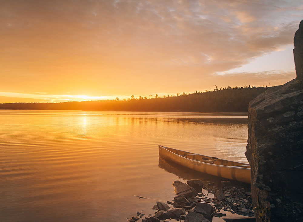 A sunset on the Boundary Waters with a canoe on the water.